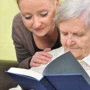 senior woman with her caregiver in home reading book