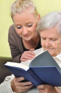 senior woman with her caregiver in home reading book