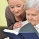 senior woman with her caregiver in home reading book